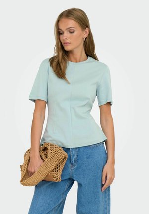 Lichtblauwe T-shirt met korte mouwen en een aansluitend ontwerp, subtiele naden en een ronde halslijn. Gekleed met losse jeans en een gevlochten tas.