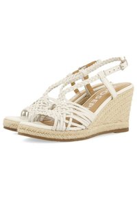 Sandalias de cuña trenzadas blancas con un detalle trenzado, que cuentan con un upper tipo lona, correa de tobillo ajustable y una suela de yute texturizada.