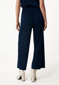 Marinblå vida byxor i texturerad ribbad tyg, med ett elastiskt midjeband. Bärs med krämfärgade klackade ankelstövlar.