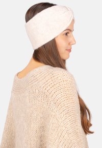 Bandeau crémé en tricot avec un design torsadé, fabriqué en laine douce, présentant une texture lisse et des variations subtiles de couleur.