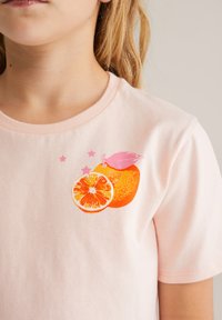 Kerge roosa puuvillane t-särk, millel on oranži viilu ja terve oranži grafika, erksate oranžide ja roosade aktsentidega ning väikeste roosade tähtedega.
