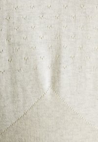 Pull crème en maille avec motifs texturés et un design côtelé diagonal en bas. Tissu doux et léger avec une légère brillance.