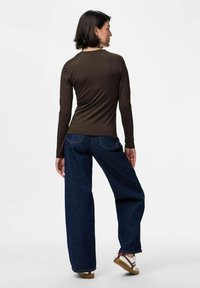 Top marrón de manga larga combinado con vaqueros holgados de color azul oscuro. Presenta un cuello redondo y una silueta relajada, acompañado de calzado casual.