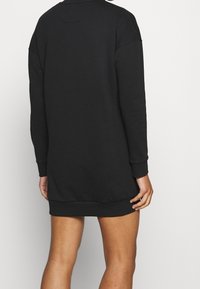 Schwarzes Sweatshirtkleid mit lockerer Passform, langen Ärmeln, gerippten Bündchen und abgerundetem Saum. Hergestellt aus weichem, strukturiertem Stoff.