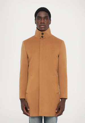 Kameelkleurige wollen jas met een hoge kraag, twee zijzakken en een voorkant met een placket met twee zwarte knopen. Gladde textuur.
