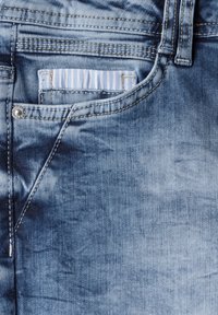 Jeans in denim blu con un dettaglio della tasca a righe blu chiaro, cuciture visibili e un bottone in metallo in vita.