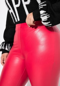 Leggings ajustati a vita alta in finta pelle lucida rosa. Maglione nero con texture presenta una scritta bianca audace e polsini a motivo.