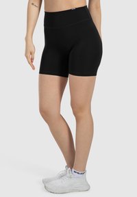 Shorts sportivi neri a vita alta con una texture liscia e elastica, caratterizzati da una lunghezza a metà coscia e dettagli di cucitura minimi.