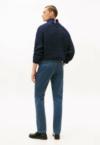 Maglione lavorato a maglia blu navy con colletto alto e accento rosso e bianco, abbinato a pantaloni turchesi e scarpe nere. Tessuto liscio e vestibilità sartoriale.