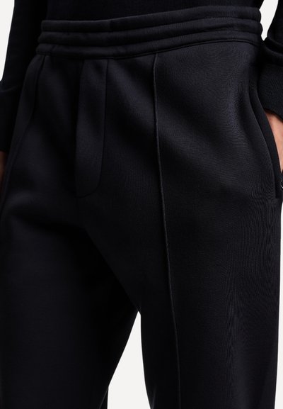 Schwarze Jogginghosen aus strukturiertem Stoff mit Seitentaschen, elastischem Bund und dezenten Nahtdetails. Elastische und figurbetonte Passform.