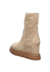 Bottines en daim beige avec talon compensé et semelle en caoutchouc crantée, présentant des coutures visibles et un bord supérieur légèrement courbé.