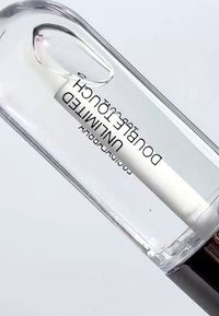 Bouteille en verre transparente étiquetée "Unlimited Double Touch" avec un bouchon noir sur fond blanc.