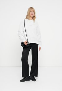 Õhuke valge sweatshirt, millel on väike logo, koos mustade laia säärega pükstega, millel on valge külgriie ja mustad spordijalatsid.