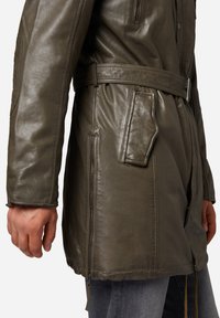 Olivgrön läderjacka med bälte i midjan, sidofickor och en lätt glänsande yta. Designad med en medellång passform.