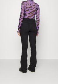 Jeans neri a campana con vita alta, abbinati a una maglietta trasparente viola con un motivo astratto marrone. Tessuto testurizzato visibile.