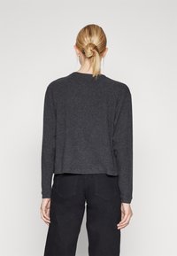 Suéter de punto en tela gris oscuro, con un ajuste relajado, mangas largas y un dobladillo redondeado. Textura suave con detalles de diseño mínimos.