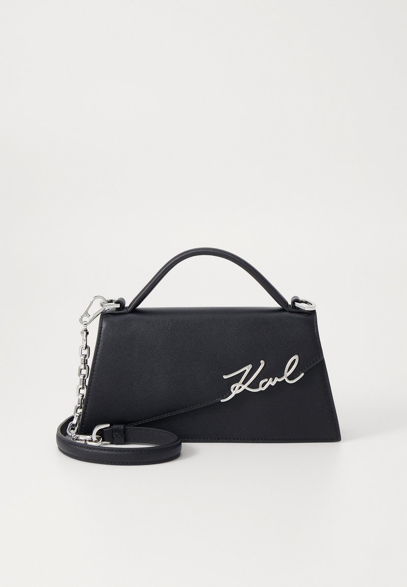 Bolso de mano de cuero negro con forma triangular, detalle del logo "Karl" en plata y cadena desmontable. Textura suave y diseño estructurado.