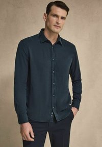 Mörkblå skjorta med knappar i ett mjukt tyg, med klassisk krage och långa ärmar, i kombination med mörka byxor. Rent design utan mönster.