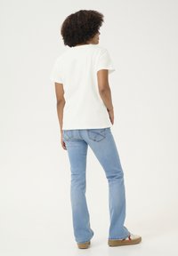 T-shirt en coton blanc, manches courtes, associé à un jean évasé bleu clair. Chaussures beiges avec des accents rouges. Design simple et décontracté.