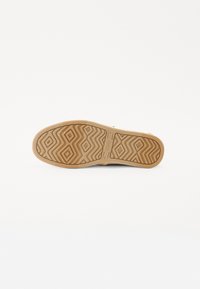 Semelle en caoutchouc avec un motif en zigzag beige. Tige en caoutchouc lisse dans une teinte neutre, présentant un branding minimal et sans embellissements supplémentaires.