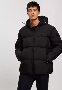 Czarna kurtka puchowa z zamkiem z przodu, kapturem i pikowanym wzorem. Posiada boczne kieszenie oraz wytłoczone logo na klatce piersiowej. Materiał: stal nierdzewna.