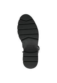 Suela de zapato de goma negra con patrones de relieve profundos, punta redondeada y marcado de la marca. El diseño enfatiza la tracción y la estabilidad.