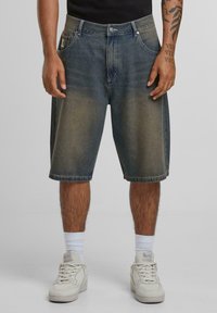 Denim shorts in a faded blue wash with a regular fit, five pockets, and a straight hem. Worn with white sneakers and ankle socks.