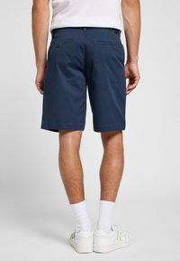 Marineblå shorts med lige pasform, lavet af let stof. Har to baglomme og knaplukning, båret med hvide sokker og sneakers.