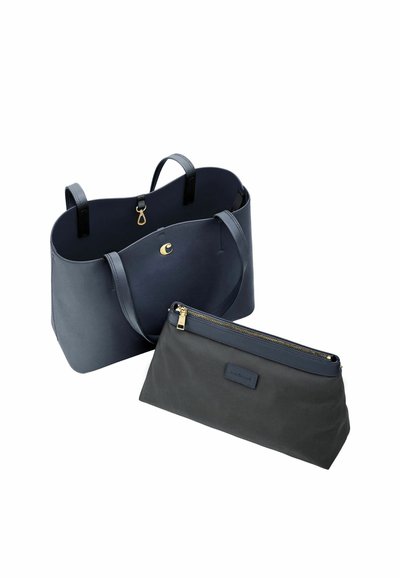 Velika temno modra torba za na rame z ramenskimi trakovi in odstranljivo temno zadrgo na sprednji strani na belem ozadju.