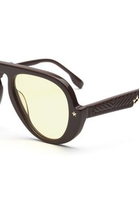 Occhiali da sole in plastica marrone con lenti gialle, forma ovale, con aste laterali marroni texturizzate e un piccolo accentato con stella dorata sul lato.