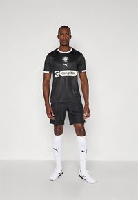 Tenue de football noire en tissu respirant avec accents blancs. Comprend un col rond, un logo et un texte sponsor ; assortie à un short noir et des chaussettes blanches.