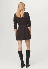 Mini płaszcz w kolorze czarnym z paskiem, wykonany z teksturowanej tkaniny, z długimi rękawami i dopasowanym krojem, zestawiony z czarnymi butami za kolano.