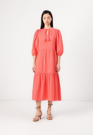 Coral maxi dress with puff sleeves, drawstring neckline, and tiered skirt. Worn with strappy nude high-heeled sandals.