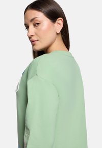 Jasnozielony sweatshirt o luźnym kroju, z haftowanymi kwiatowymi detalami na rękawach i okrągłym dekoltem. Miękka tekstura.