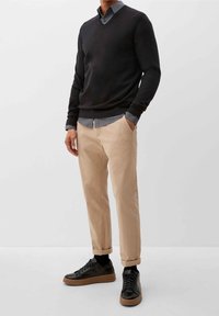 Schwarzer V-Ausschnitt-Pullover über einem blauen karierten Hemd, beigen Chinos und schwarzen Sneakers mit einer hellbraunen Sohle; lässiges, geschichtetes Outfit.