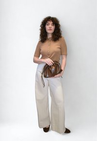 Polo marron à manches courtes avec boutons, pantalon large crème, et sac à cordon en cuir marron foncé. Textures lisses et couleurs neutres.