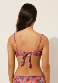 Flerfärgad bikini med en volang bakrem och snörning. Har livliga mönster i nyanser av rosa, lila och blå.