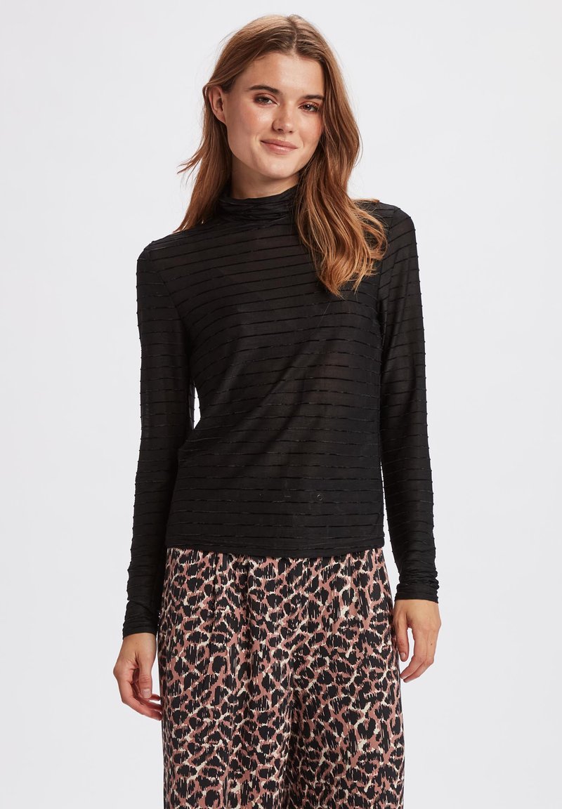 Schwarzes Langarmshirt mit einem strukturierten, gestreiften Muster und einem Stehkragen. Kombiniert mit rosa Hollandtuch-Hosen mit Leopardenmuster.