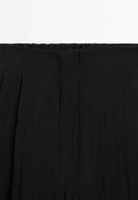 Jupe noire avec tissu texturé et froissé. Taille élastique et design plissé visibles. Aucun autre détail ou motif apparent.