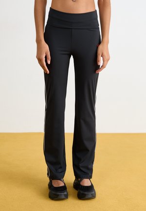 Black athletic pants with a high waistband, white side stripes, and a smooth, stretchy texture. Features a concealed side pocket.