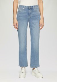 Jeans en denim bleu clair, à jambe droite. Comprend cinq poches et une fermeture à bouton à l'avant. Portés avec des baskets blanches à plateforme.