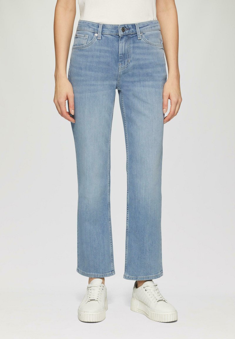 Jeans en denim bleu clair, à jambe droite. Comprend cinq poches et une fermeture à bouton à l'avant. Portés avec des baskets blanches à plateforme.