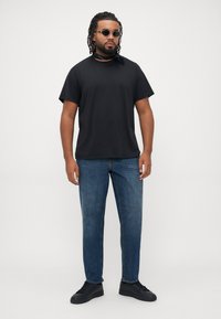 Black cotton t-shirt, blue denim jeans, black sneakers, and sunglasses. Individual wears a black neck scarf and has curly hair.