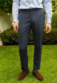 Mørkeblå skræddersyede bukser med subtil tekstur, glat front og slim fit. Parret med brune ruskindssko for et poleret udseende.