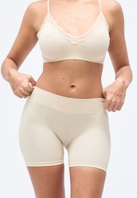 Ensemble de lingerie beige comprenant un bralette orné de dentelle et un short mi-cuisse lisse avec une large ceinture élastique, présentant un design sans coutures.