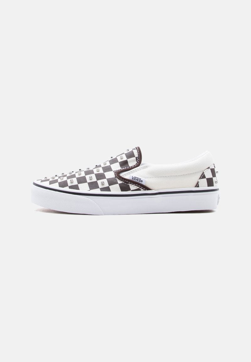 Alacsony szárú, fekete-fehér sakktáblamintás Vans slip-on cipő, fém szegecsekkel a felsőrészén, fehér gumitalppal és Vans logós címkével az oldalán.