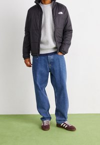 Chaqueta negra acolchada, suéter gris, jeans holgados azules y zapatillas burdeos con rayas blancas. Tela suave, ajuste relajado y detalle de cremallera.