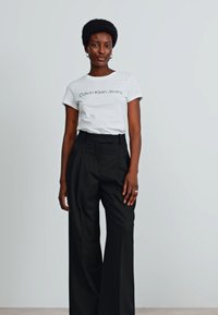 Witte katoenen t-shirt met "Calvin Klein Jeans" in het zwart gedrukt, gecombineerd met zwarte broek met hoge taille en wijde pijpen. Glad textuur, minimalistisch ontwerp.