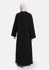 Long black fabric dress with wide sleeves and a straight cut, featuring a simple design and smooth texture. Back view shows a modest silhouette.
