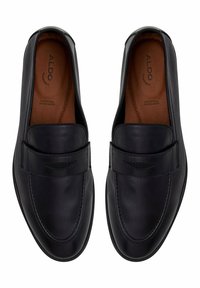 Chaussures en cuir noir à enfiler avec un bout rond et une semelle plate, présentant un accent cousu sur l'empeigne et une texture lisse et polie.